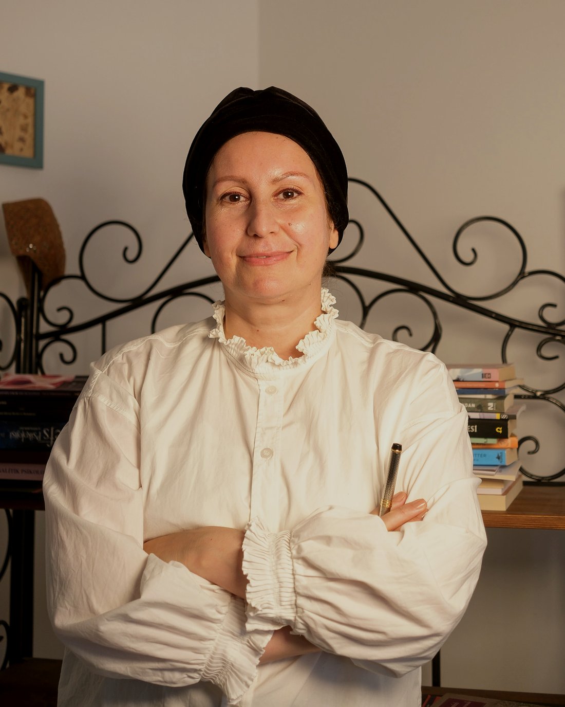 Dilek Karadağ — kütüphanesinin önünde, elinde kalemiyle